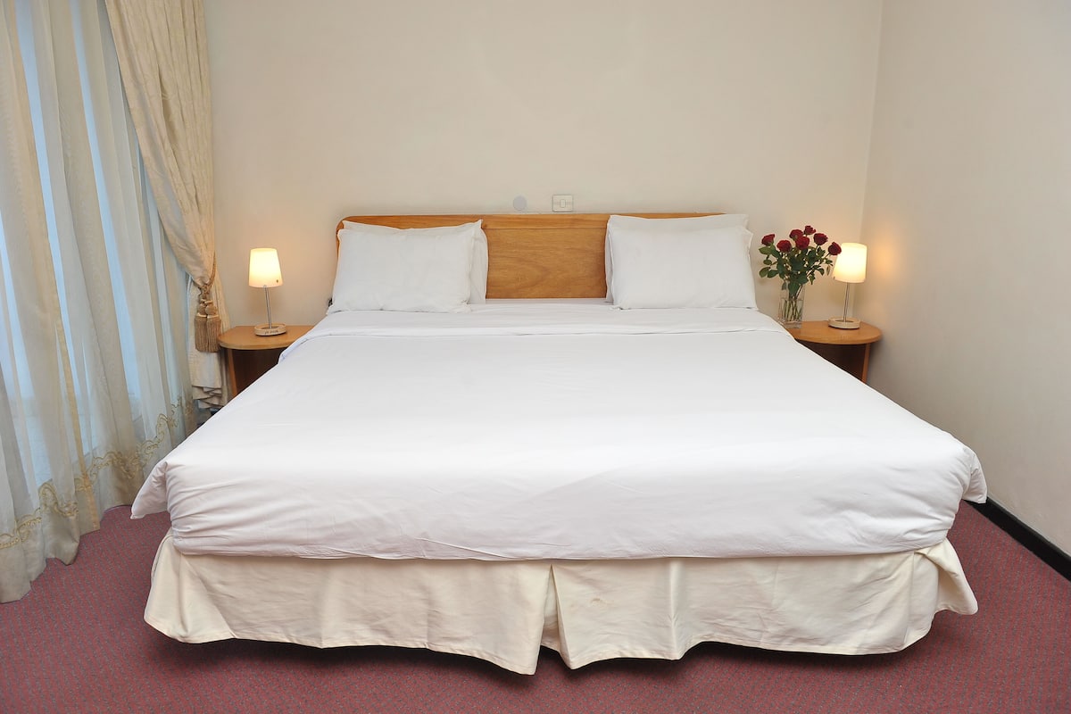 A neatly made bed with white linens, two bedside tables with lamps, and a vase with flowers on one table.