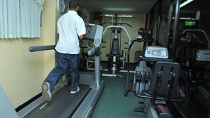 En mand træner på løbebånd i et fitnesscenter med forskellig træningsudstyr.