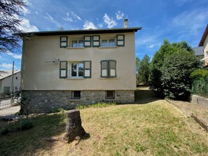 Un edificio de dos pisos con base de piedra y techo plano, con múltiples ventanas y contraventanas.