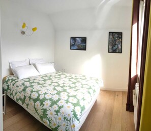 Un dormitorio con cama, paredes blancas y dos cuadros en la pared.