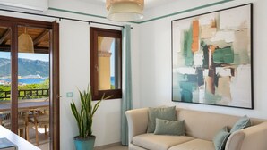 Een moderne woonkamer met een beige bank, een groot abstract schilderij en uitzicht op zee door een glazen deur.