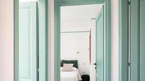 Een gang die leidt naar een slaapkamer met een bed, nachtkastje en een wandlamp.