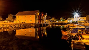 A waterfront property with a large building, a dock with boats, and a calm water body reflecting the structures. - Glesvær Rorbu (Oygarden)