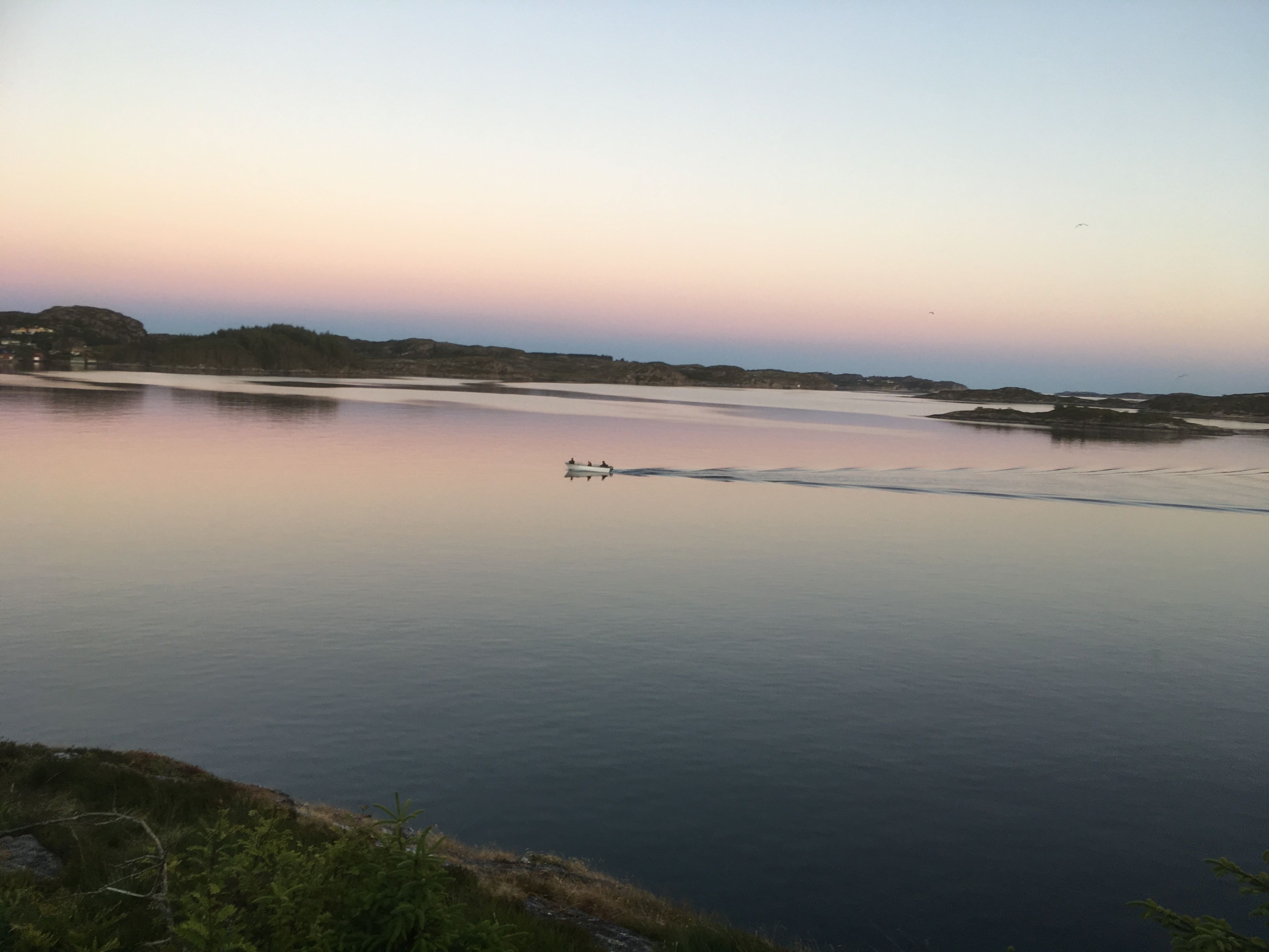 A calm river with a boat in the middle, surrounded by hills and sparse vegetation.