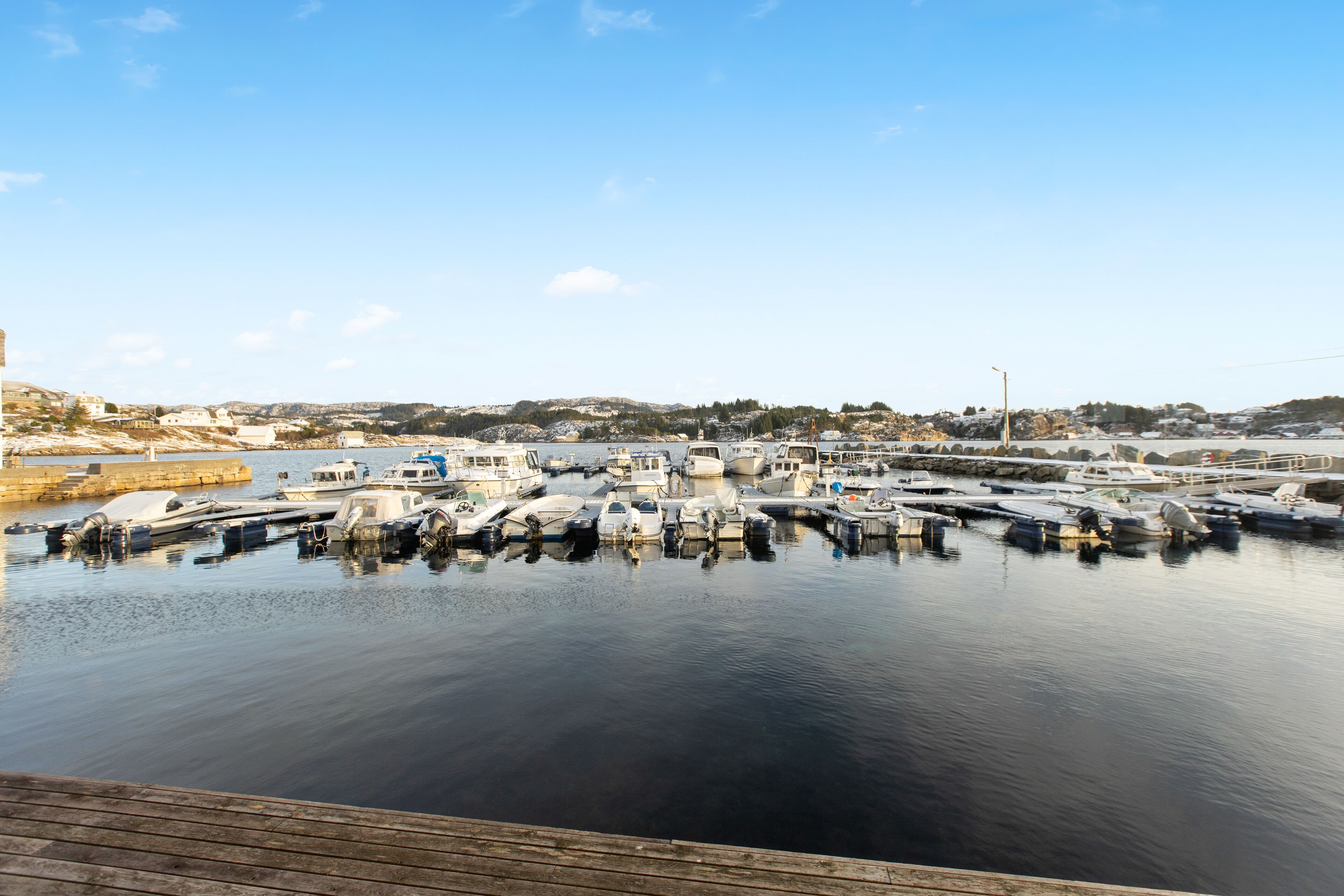 A marina with multiple boats docked, a wooden dock, and a clear sky.