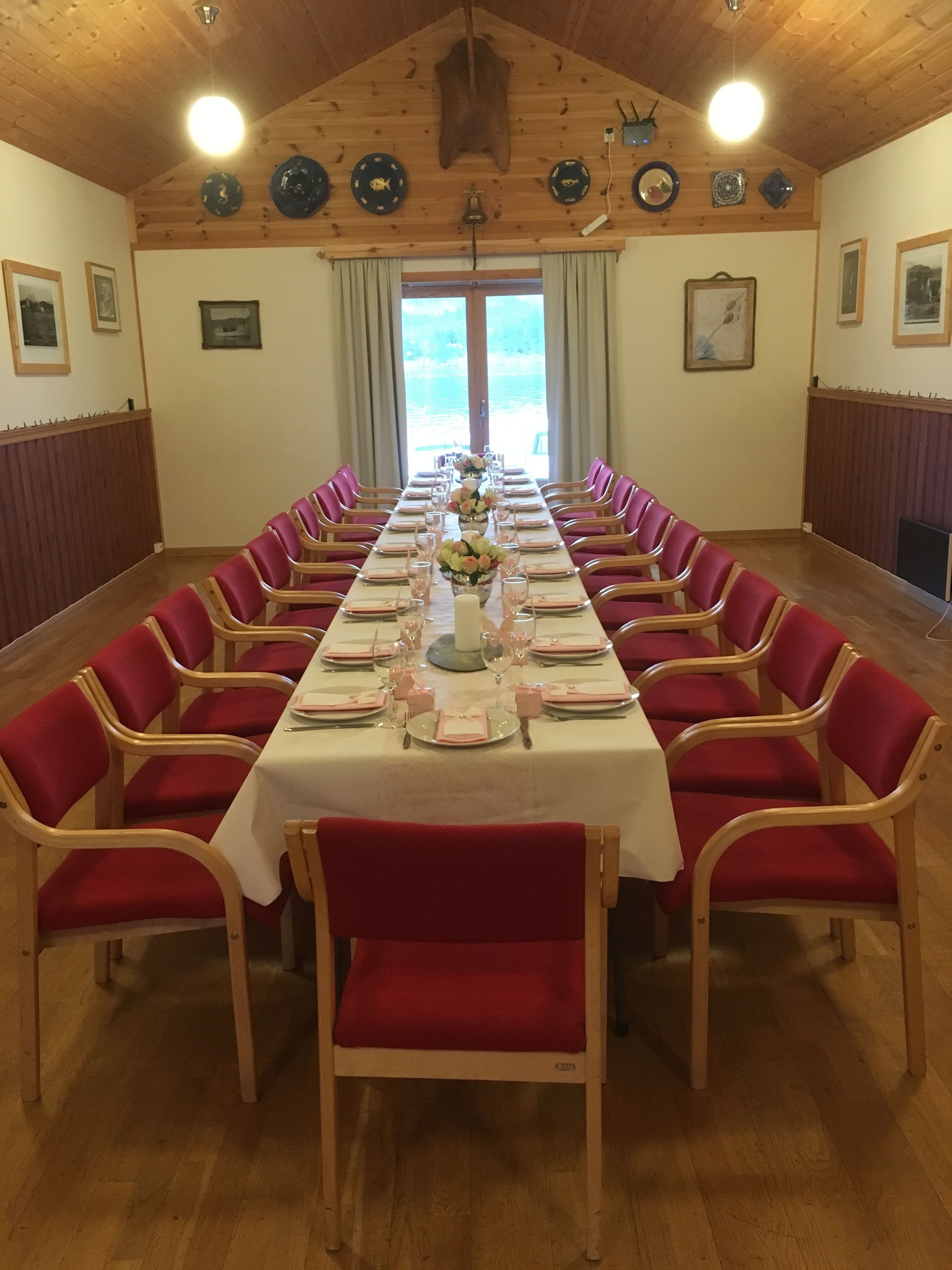 A long dining table set for a meal with red upholstered chairs, centered with a floral arrangement.