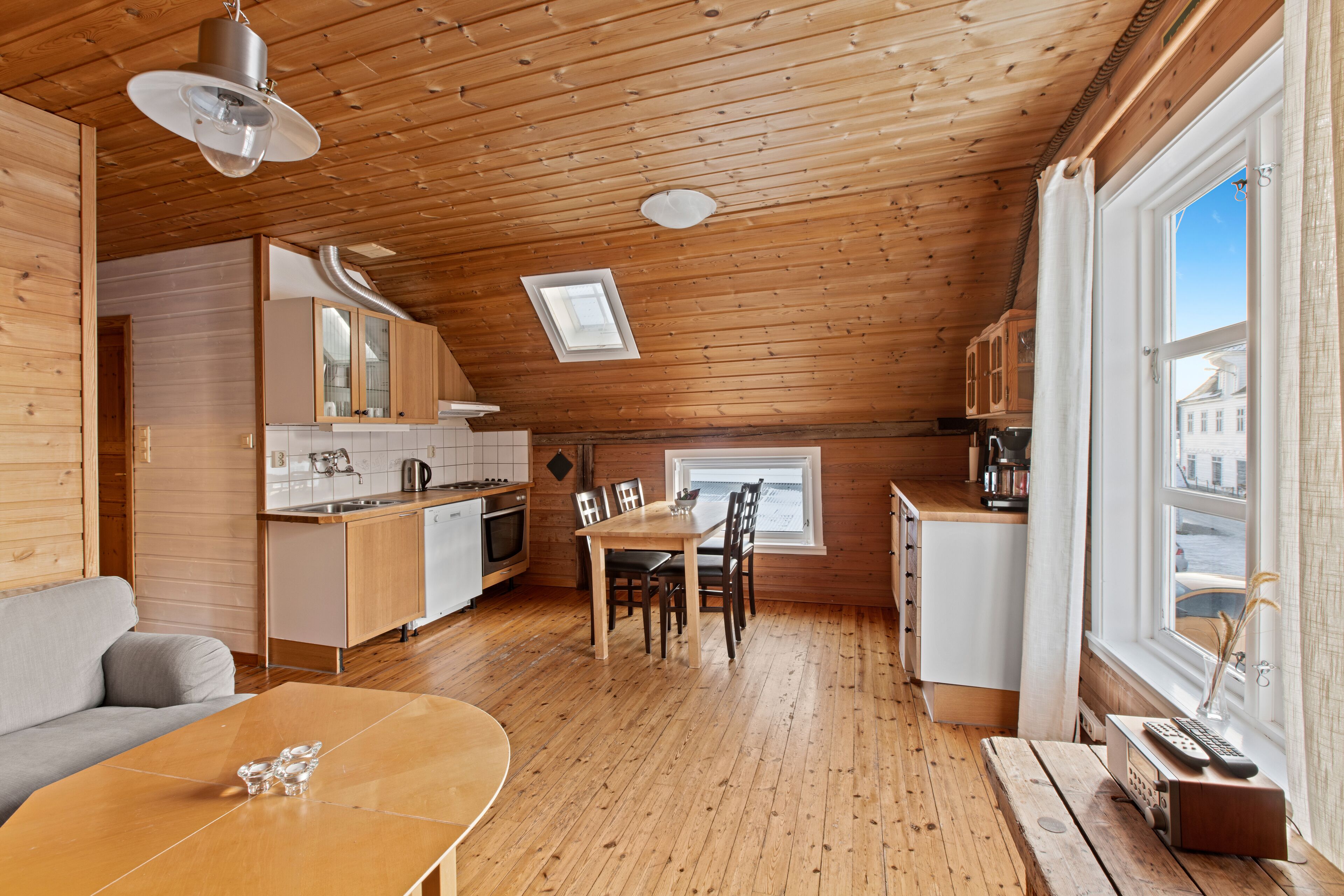 A cozy wooden cabin with a dining area, kitchen, and a large window offering a view.