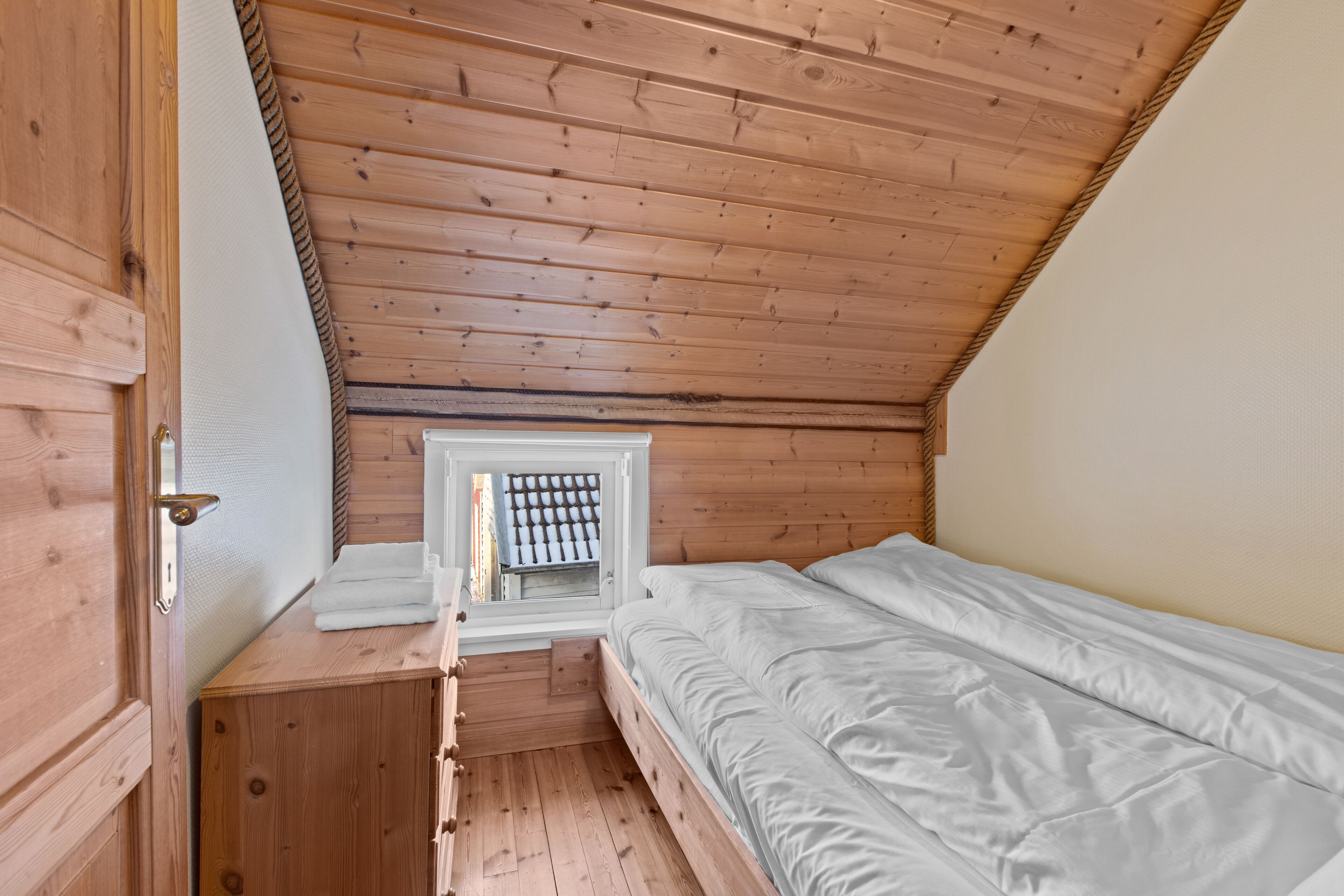 Una habitación pequeña con paneles de madera, una cama individual, una ventana con vistas y un aparador de madera.