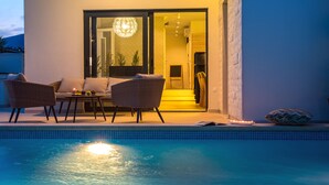 Un espace aménagé au bord de la piscine, avec des meubles en osier, une porte vitrée donnant sur un intérieur lumineux et une piscine carrelée.