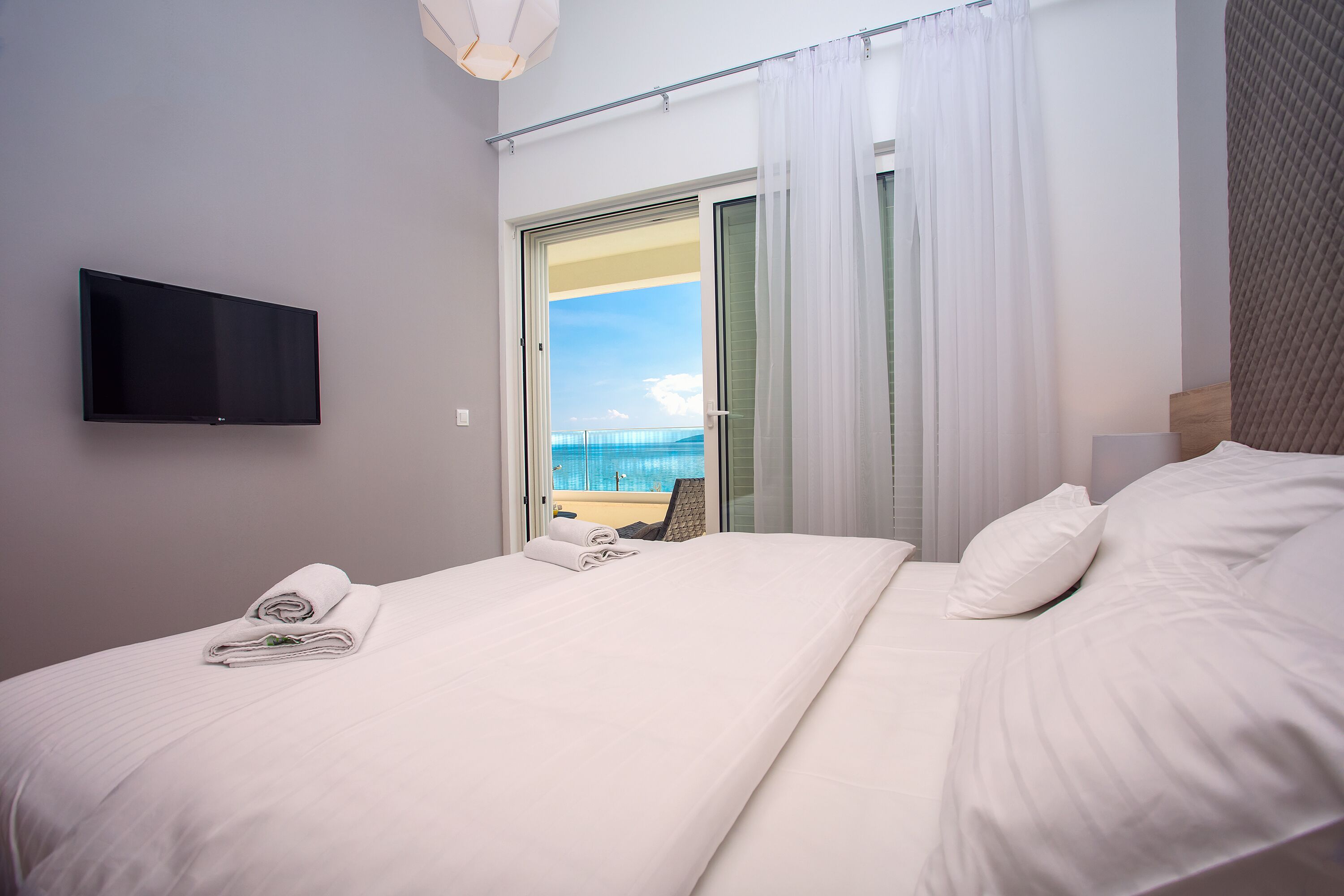 Une chambre d’hôtel avec un lit, un téléviseur fixé au mur et une vue sur la mer, visible à travers une porte vitrée.