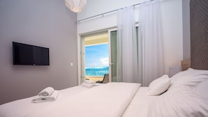 Une chambre d’hôtel avec un lit, un téléviseur fixé au mur et une vue sur la mer, visible à travers une porte vitrée.