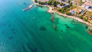 Vue aérienne d’une zone côtière avec des eaux turquoise limpides, une jetée et un quartier résidentiel avec des bâtiments et de la végétation.