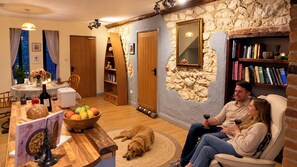 A cozy living room with a dog, a fireplace, a bookshelf, and a dining area with a table set for two.