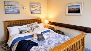 A neatly made bed with a blue floral bedspread, a pillow with 'Life is Good' text, and a lamp on a bedside table.