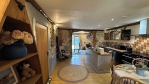 A cozy kitchen with a stone wall, wooden shelves, and a dining area with a round rug. - The Old Barn Self Catering Cottage by the Beach, Dog Friendly on Norfolk Coast (Heacham)