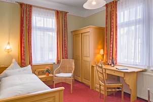 Habitación de hotel con cama, escritorio, silla, armario y ventana con cortinas.