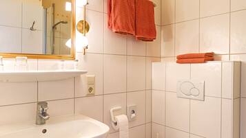A bathroom with a white sink, mirror, and toilet. There are orange towels hanging on the wall.