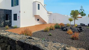 A modern white building with a stone facade, a wooden deck, and a landscaped garden with rocks and plants. - Villa Vicini - with Pool Table & Private Pool in Great Location (Playa Blanca)
