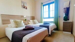 A hotel room with two beds, a nightstand, a dresser, and a window with curtains. - Villa Vicini - with Pool Table & Private Pool in Great Location (Playa Blanca)