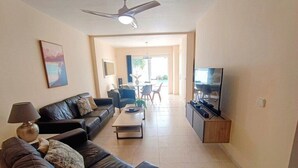 A modern living room with a sofa, coffee table, TV, and a dining area in the background. - Villa Vicini - with Pool Table & Private Pool in Great Location (Playa Blanca)