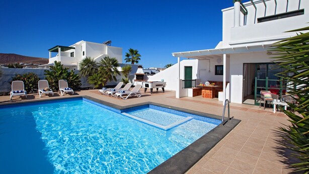 A swimming pool with lounge chairs, a sun terrace, and white buildings in the background. - Villa Vicini - with Pool Table & Private Pool in Great Location (Playa Blanca)