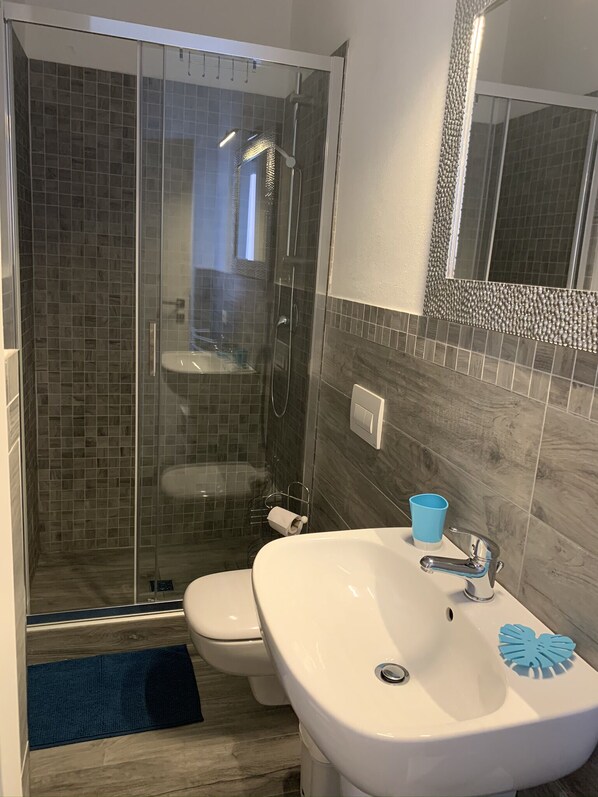 Ein Badezimmer mit einer Duschkabine, einem weißen Waschbecken und einem Seifenspender in Herzform in Blau sowie einer Toilette.