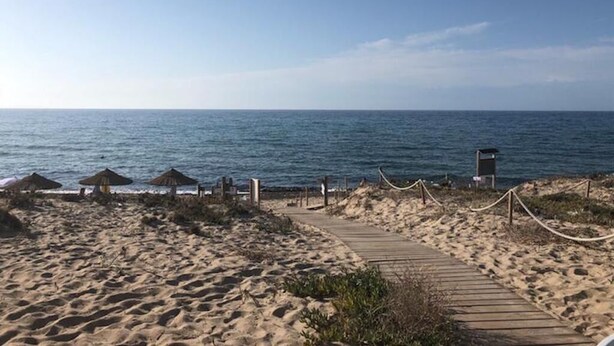 A sandy beach with a wooden pathway leading to the sea, a lifeguard tower, and thatched umbrellas. - Tulipano House - Key to Villas (La Ciaccia)