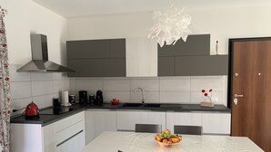 A modern kitchen with a central island, a dining table with chairs, and a large pendant light. - Tulipano House - Key to Villas (La Ciaccia)