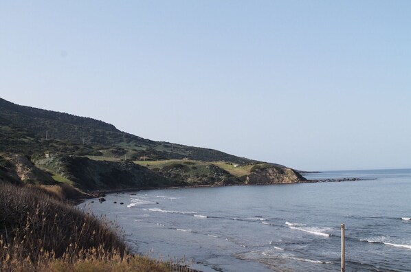 A coastal landscape with a beach, grassy hills, and a clear sky.