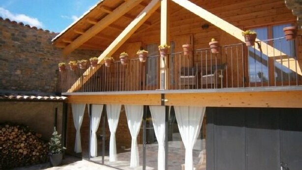 A wooden balcony with potted plants, white curtains, and a stone wall in the background. - L'Estisora de Casa l'Hereu for 8 people (Baix Pallars)