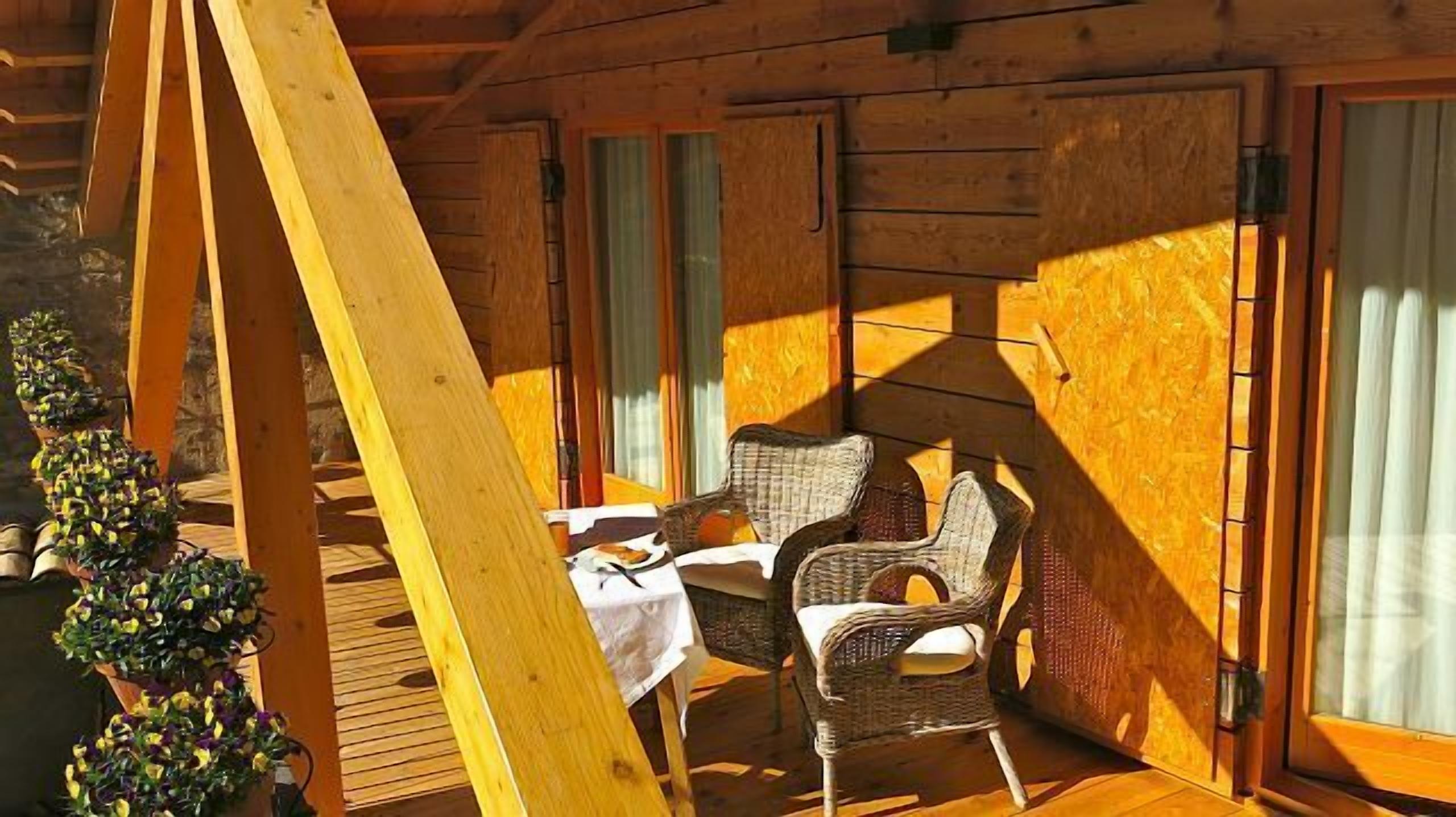 A wooden cabin with a dining table and wicker chairs, large windows, and a wooden deck.