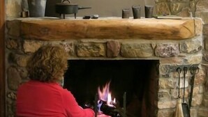 A stone fireplace with a wooden mantel, a woman sitting in front of it, and a fire burning inside. - L'Estisora de Casa l'Hereu for 8 people (Baix Pallars)