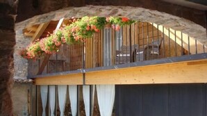 A rustic stone archway leading to a wooden balcony with hanging flower baskets. - L'Estisora de Casa l'Hereu for 8 people (Baix Pallars)