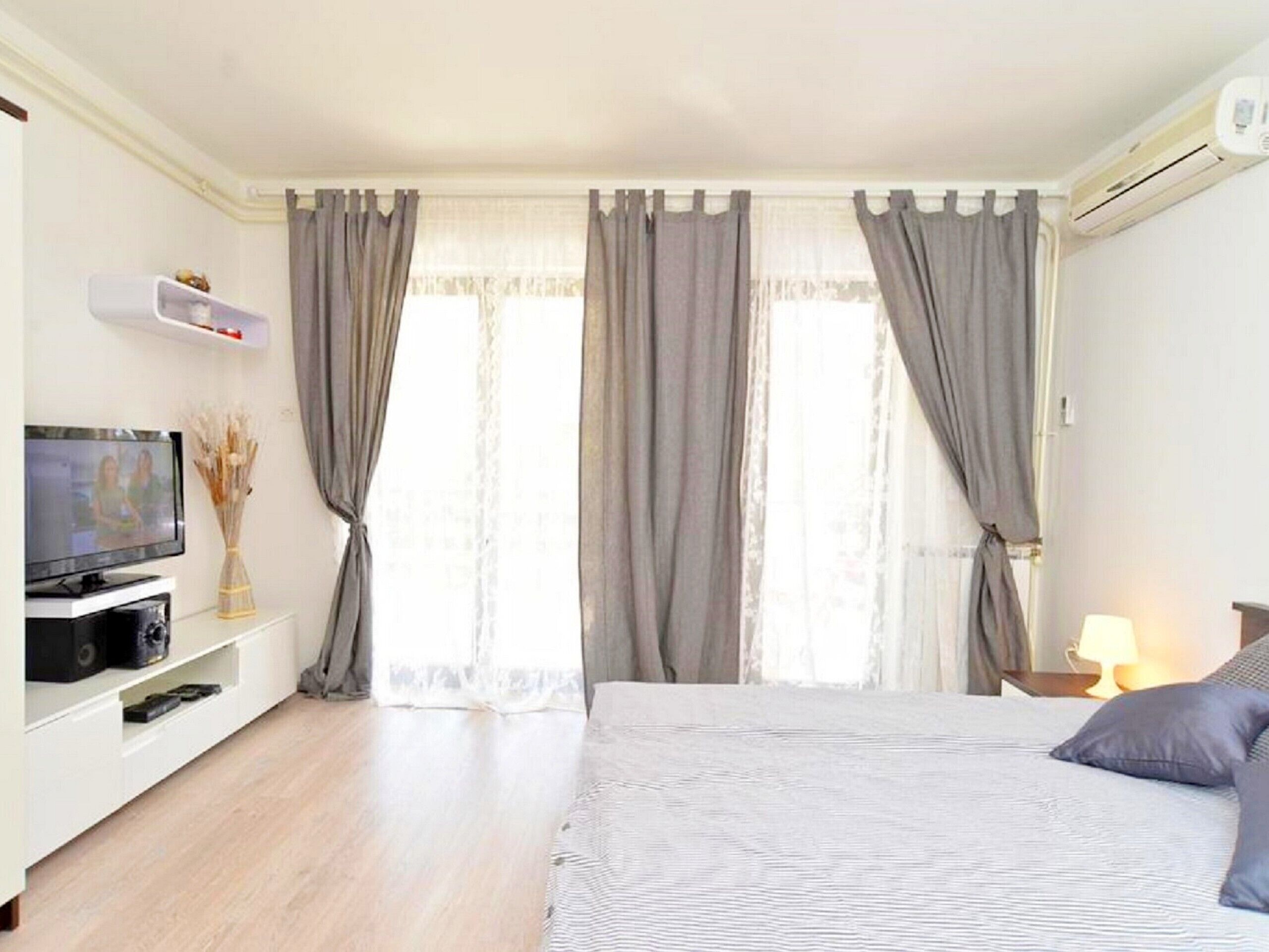 A hotel room with a bed, a TV, a shelf with decorative items, and a window with curtains.