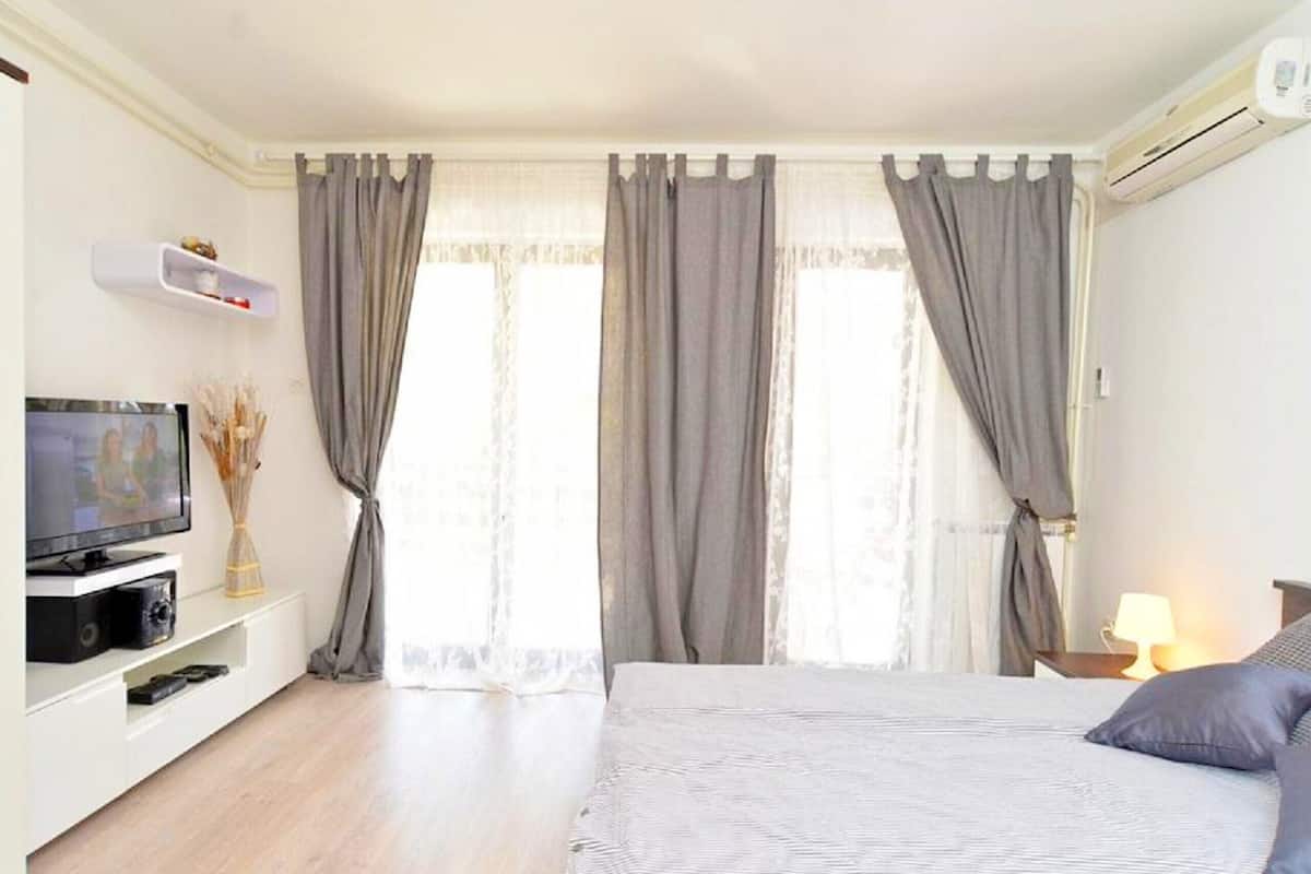 A hotel room with a bed, a TV, a shelf with decorative items, and a window with curtains.