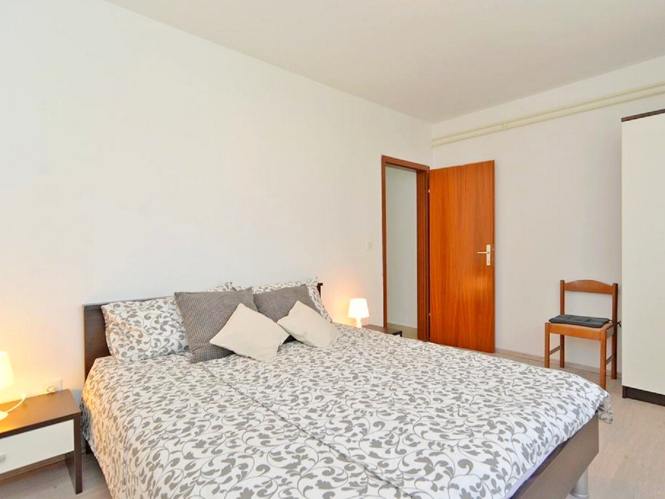 A bedroom with a bed, bedside tables, a chair, and a wardrobe.
