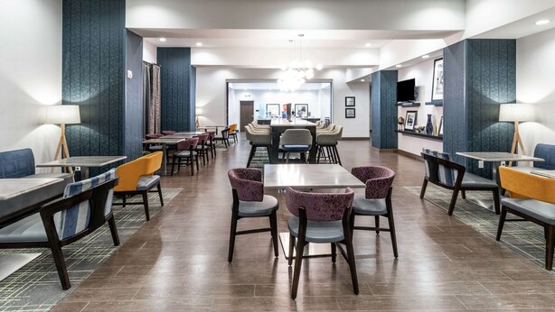 Eine geräumige Hotelhalle mit mehreren Sitzbereichen, einem zentralen Esstisch und einem Fernseher an der Wand.