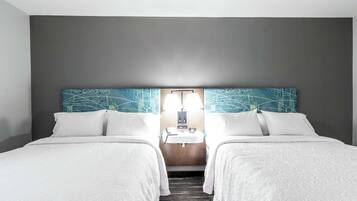 A hotel room with two beds, a nightstand, a mirror, and a wall-mounted light fixture.