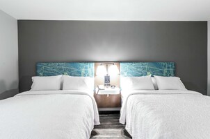 Habitación de hotel con dos camas, una mesita de noche, un espejo y una lámpara fijada a la pared.