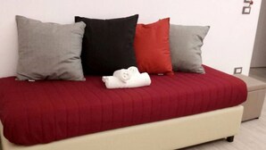 A bed with a red bedspread, three pillows in grey, black, and red, and a white towel on the bed.