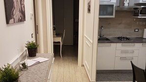 A modern kitchen with a central island, a dining area with a chair, and a hallway leading to a bedroom.