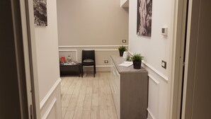 A hallway with a reception desk, a chair, and two potted plants.