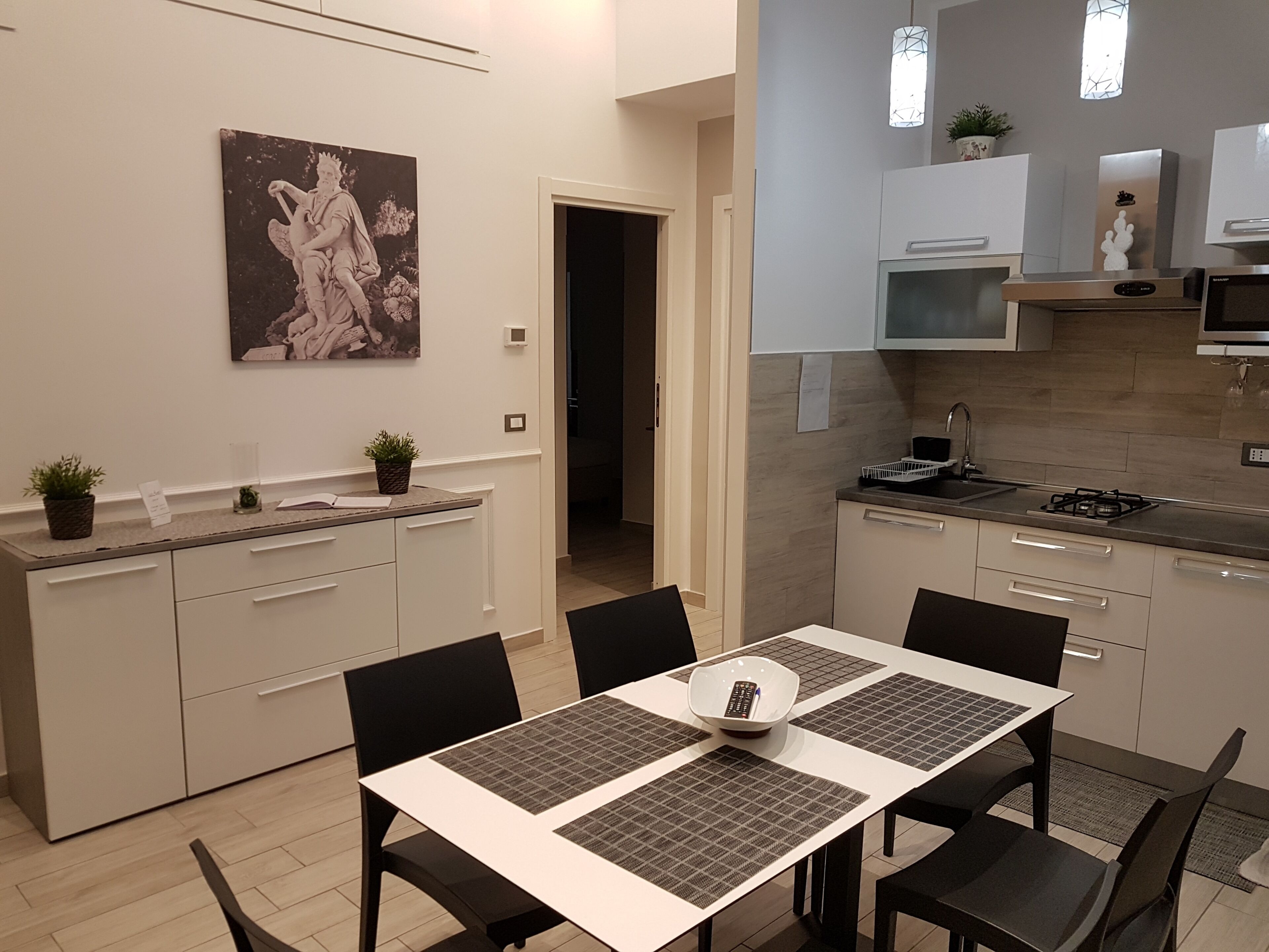 A modern kitchen with white cabinets, a dining table with black chairs, and a decorative painting on the wall.