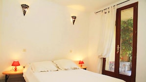 A bedroom with a bed, two bedside lamps, a door with a view, and a small table.