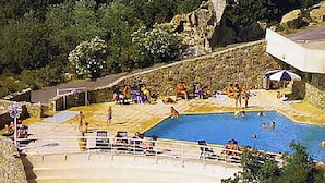 A swimming pool with people around it, a beach area, and some greenery in the background.