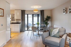 A modern living room with a sofa, a dining table with chairs, and a kitchen area with cabinets and a refrigerator. - Fantastic 3-bed house in Bath with free parking (BATH)