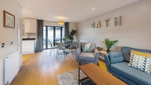 Una sala de estar moderna con un sofá, una mesa de centro y un comedor con sillas y una mesa. Hay una cocina con armarios y una ventana.