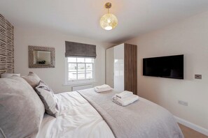 A bedroom with a bed, a television, a window with blinds, a mirror, and a wall-mounted light fixture. - Fantastic 3-bed house in Bath with free parking (BATH)