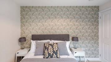 A bedroom with a patterned wallpaper, a bed with pillows, a bedside table, and a nightstand.