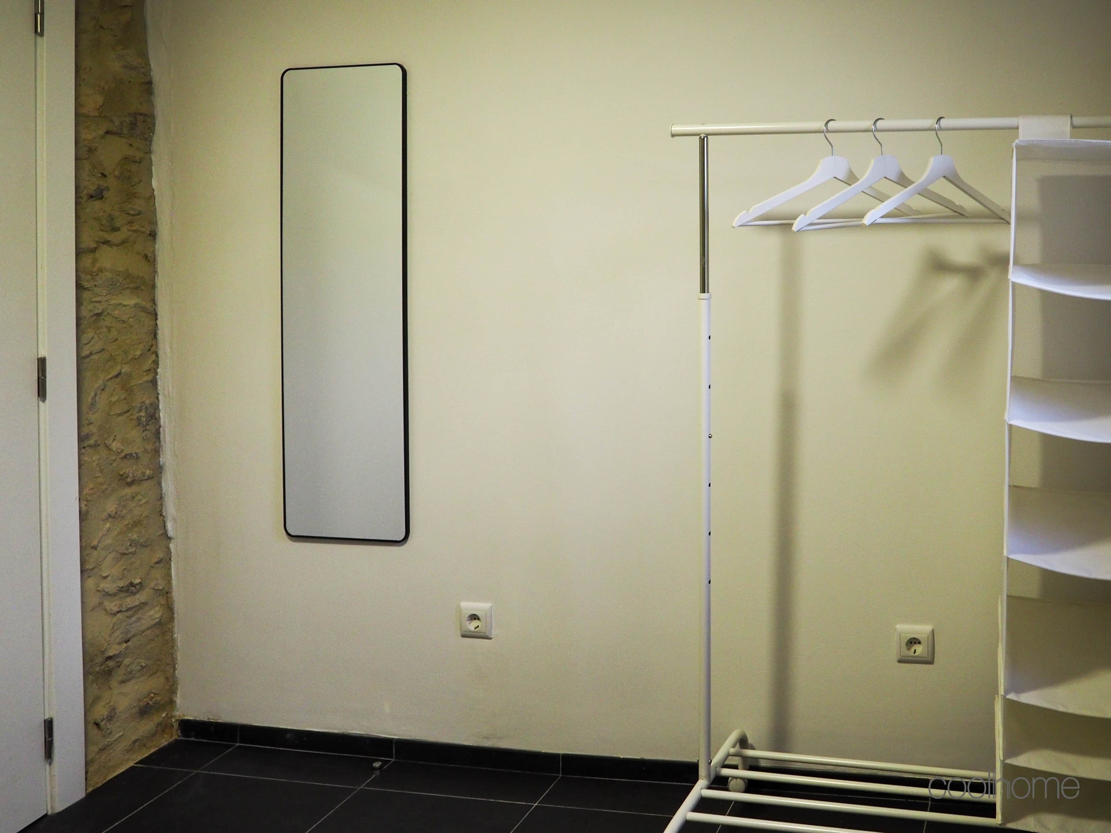 Une pièce avec un mur blanc, un mur en pierre servant d’élément décoratif, un portant à vêtements blanc suspendu et une étagère blanche.